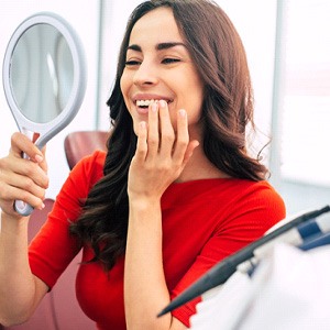 Woman in red shirt checking smile in handheld mirror