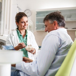 Smiling dentist showing patient model of teeth