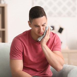 Young man holding cold compress to sore face