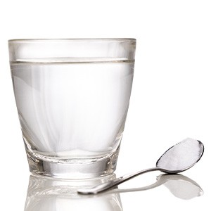 Clear glass of water next to spoonful of salt on reflective surface