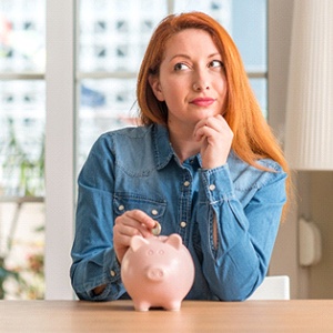 Woman putting coin in piggy bank for dental emergency in Dallas