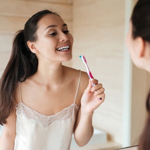 Woman brushing teeth to prevent dental emergency in Dallas