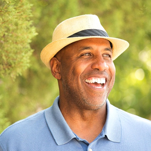 man in blue polo and fedora smiling with dental implants in North Dallas