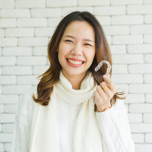 woman in white sweater holding aligner in front of white brick wall