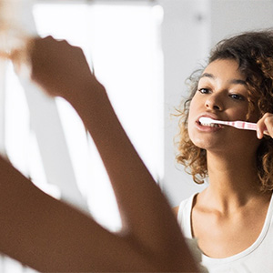 woman brushing teeth to prevent dental emergencies in Dallas