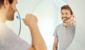 Smiling man holding toothbrush in front of mirror