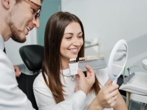Woman looking into mirror with dentist holding up dental veneer model.