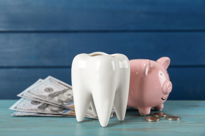 A large ceramic tooth next to dollar bills and a piggy bank